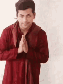 a man in a red shirt is standing with his hands folded and smiling .