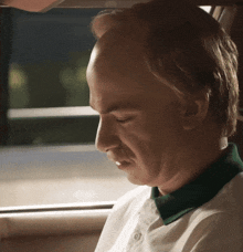 a bald man with a green collar is sitting in a car with his eyes closed