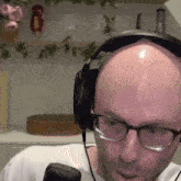 a bald man wearing glasses and headphones looks at something