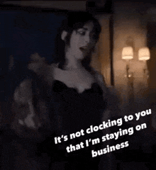 a woman in a black bra and jacket is standing in a dark room with a clock on the wall .
