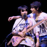 a man in a onew shirt is hugging another man who is holding a guitar .