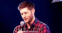 a man in a plaid shirt is smiling while holding a microphone and saying well , thank you .