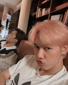 a man with pink hair is making a face while another man sleeps on a couch