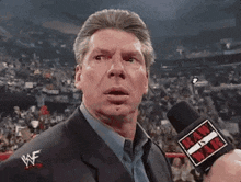 a man in a suit and tie is talking into a microphone in a stadium .