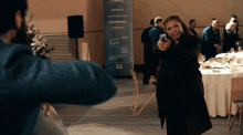 a woman is pointing a gun at a man in front of a sign that says ' the international anti-corruption conference '