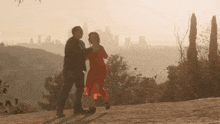 a man and woman are dancing on a hill with a city skyline in the background