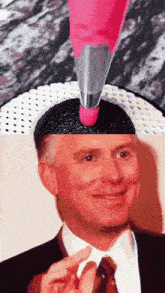 a man in a suit and tie is smiling while a pink piping bag is being used to decorate a cake