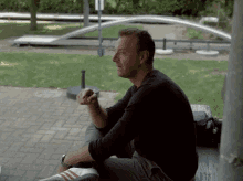 a man in a black shirt sits on a brick sidewalk