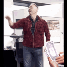 a man in a red jacket is dancing in front of a stack of money