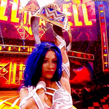 a woman with blue hair is holding a wrestling championship belt over her head
