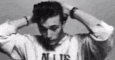 a black and white photo of a young man holding his hair in his hands .