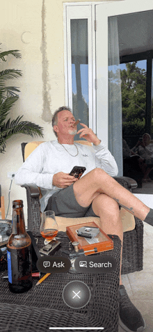a man is sitting in a chair smoking a cigar while looking at his phone