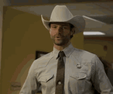 a man in a cowboy hat and tie is standing in a room .