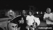 a black and white photo of a group of young men standing in front of a white car .
