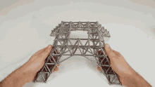 a person is holding a metal structure in their hands that looks like a bridge
