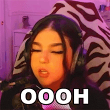 a girl wearing headphones is sitting in front of a microphone with her eyes closed and the word oooh on her face .