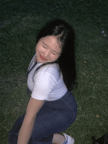 a girl in overalls and a white shirt is squatting down in the grass