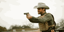 a man in a cowboy hat holds a gun in his right hand
