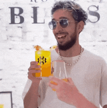 a man wearing sunglasses and a pearl necklace is holding a drink in front of a wall that says bliss