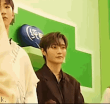a man in a suit is standing next to another man in a room with a green wall .