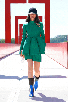 a woman in a green dress and blue boots is walking on a bridge