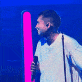a man is singing into a microphone on a stage in front of a pink and blue light .