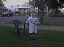 a boy in a white shirt is jumping in the grass next to a chair .