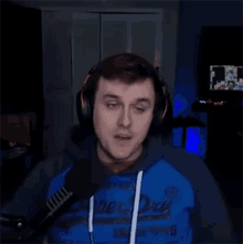 a man wearing headphones and a blue hoodie is standing in front of a microphone in a dark room .