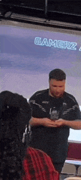 a man in a black shirt is standing in front of a screen with the word gamerz on it .