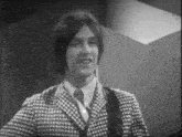a man in a plaid suit and tie is smiling in a black and white photo