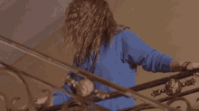 a woman wearing sunglasses and a blue sweater is standing on a set of stairs with her hair blowing in the wind .