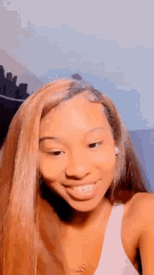 a young woman with long brown hair is smiling for the camera while wearing a white tank top .