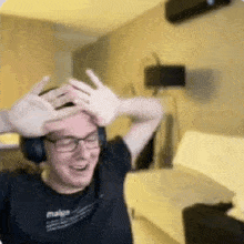 a man wearing headphones and glasses is making a funny face while holding his hands on his head .