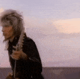 a man in a leather jacket is playing a guitar on a beach .