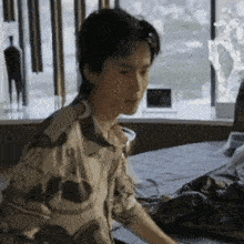 a man is sitting on a bed in front of a window looking at something .