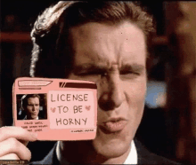 a man in a suit holds up a pink sticker that says license to be horny