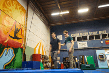 two men are standing in a gym with a sign that says circus is for every body