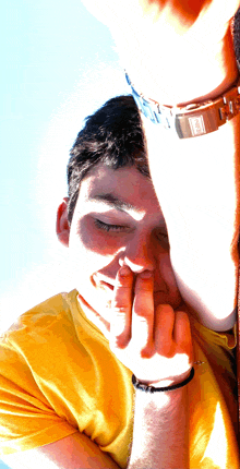 a man in a yellow shirt has his hand on his face and a watch on his wrist