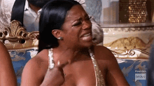 a woman is crying while sitting on a couch in a gold dress .