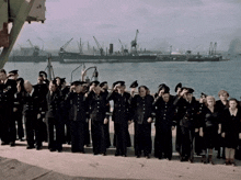 a large group of people in black uniforms salute in front of a body of water
