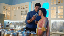 a man and woman are in a kitchen looking at jars