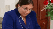a woman wearing glasses and headphones is sitting in front of a vase of red roses .