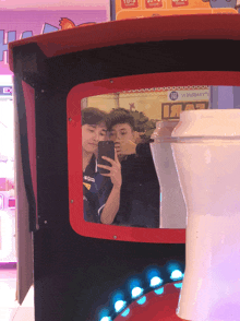 two boys taking a picture of themselves in an arcade machine