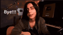 a young man with long hair is sitting in front of a guitar and waving his hand .