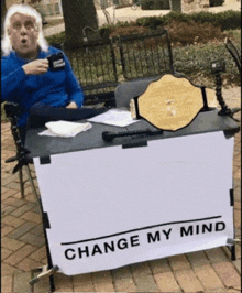 a man sitting at a table with a sign that says change my mind on it