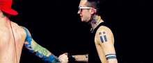 two men with tattoos on their arms are shaking hands .