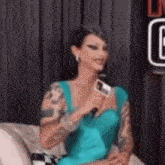 a woman with tattoos is sitting on a couch holding a microphone .