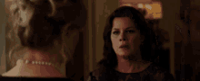 a woman with a pearl necklace is talking to another woman in a room .