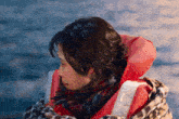 a woman wearing a red life jacket and scarf looks to the side