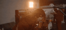 a man is singing into a microphone in a dark room while a drummer plays drums in the background .